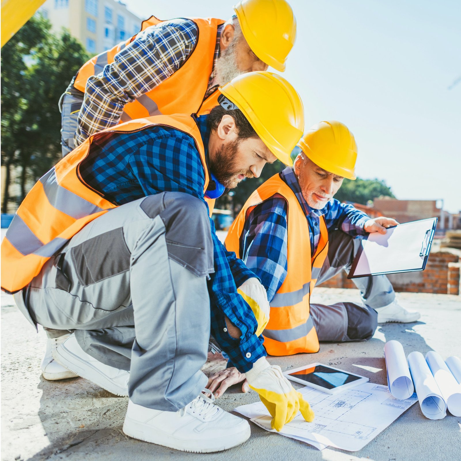handsome construction workers sitting on concrete at construction site, discussing building plans